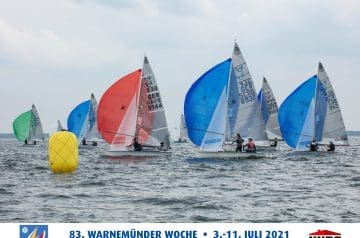 Yachtreise mit mehreren Segelbooten mit bunten Segeln in der offenen See bei bewölktem Himmel, umkreist von einer gelben Boje, während eine Regatta stattfindet.