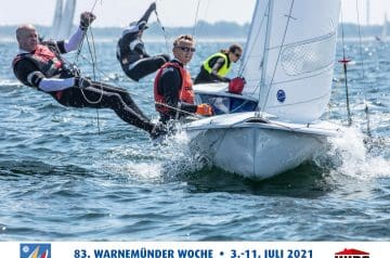 Vier Segler auf einem weißen Segelboot bei einer Regatta im Wasser, alle mit Schwimmwesten, das Boot hat eine große Prise an einem Segel, im Hintergrund ein offenes Wassermeer und ein blauer Himmel