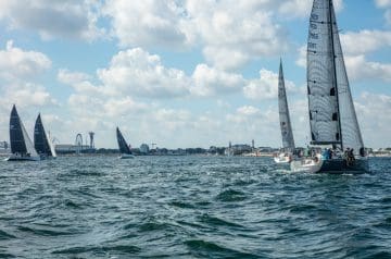 Mehrere Segelboote auf dem Wasser während einer Regatta vor einer Stadt mit Wolken am Himmel