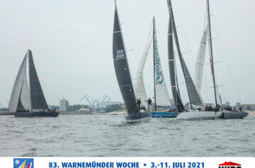 Mehrere Segelboote auf dem Wasser während der Warnemünder Woche vom 3. bis 11. Juli 2021, mit großem Hafen im Hintergrund.